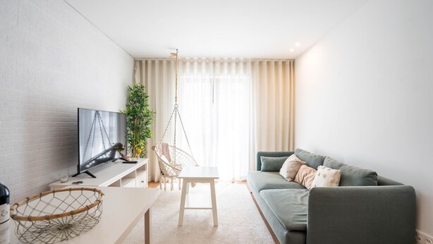 Uma sala de estar moderna com televisão de tela plana, uma cadeira suspensa, um sofá e uma mesinha com um objeto decorativo.
