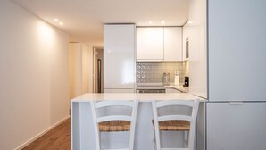 Uma cozinha moderna com armários brancos, uma ilha central com duas cadeiras e painel de azulejos.