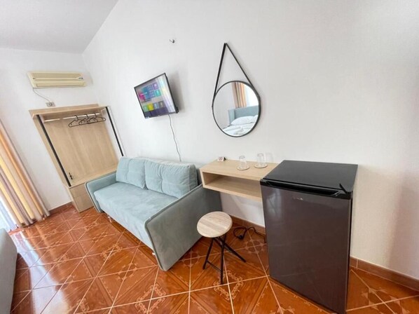 A compact room with a sofa, a small table, a refrigerator, a mirror, and a TV.