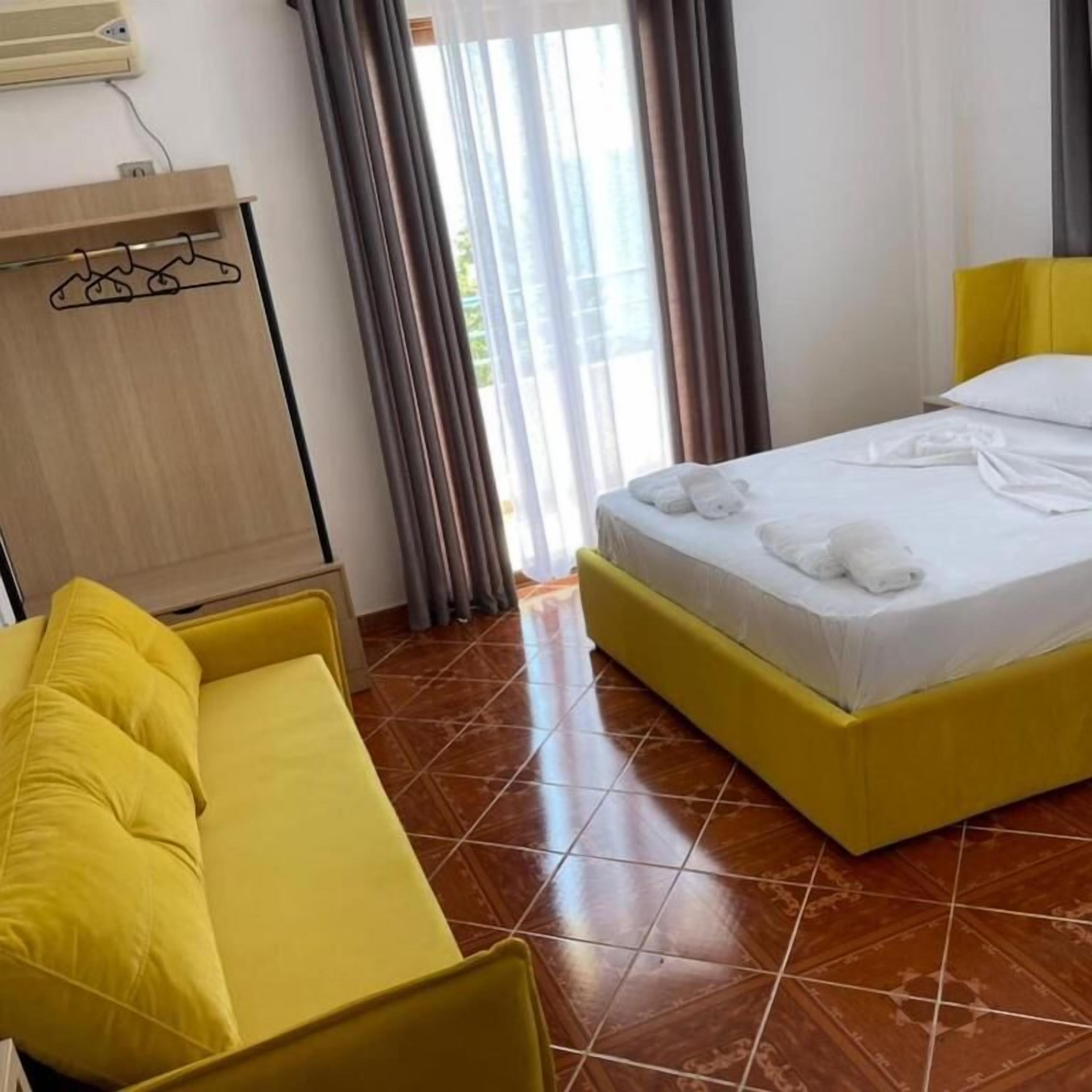 A hotel room with a yellow bed, a yellow sofa, and a wooden wardrobe.