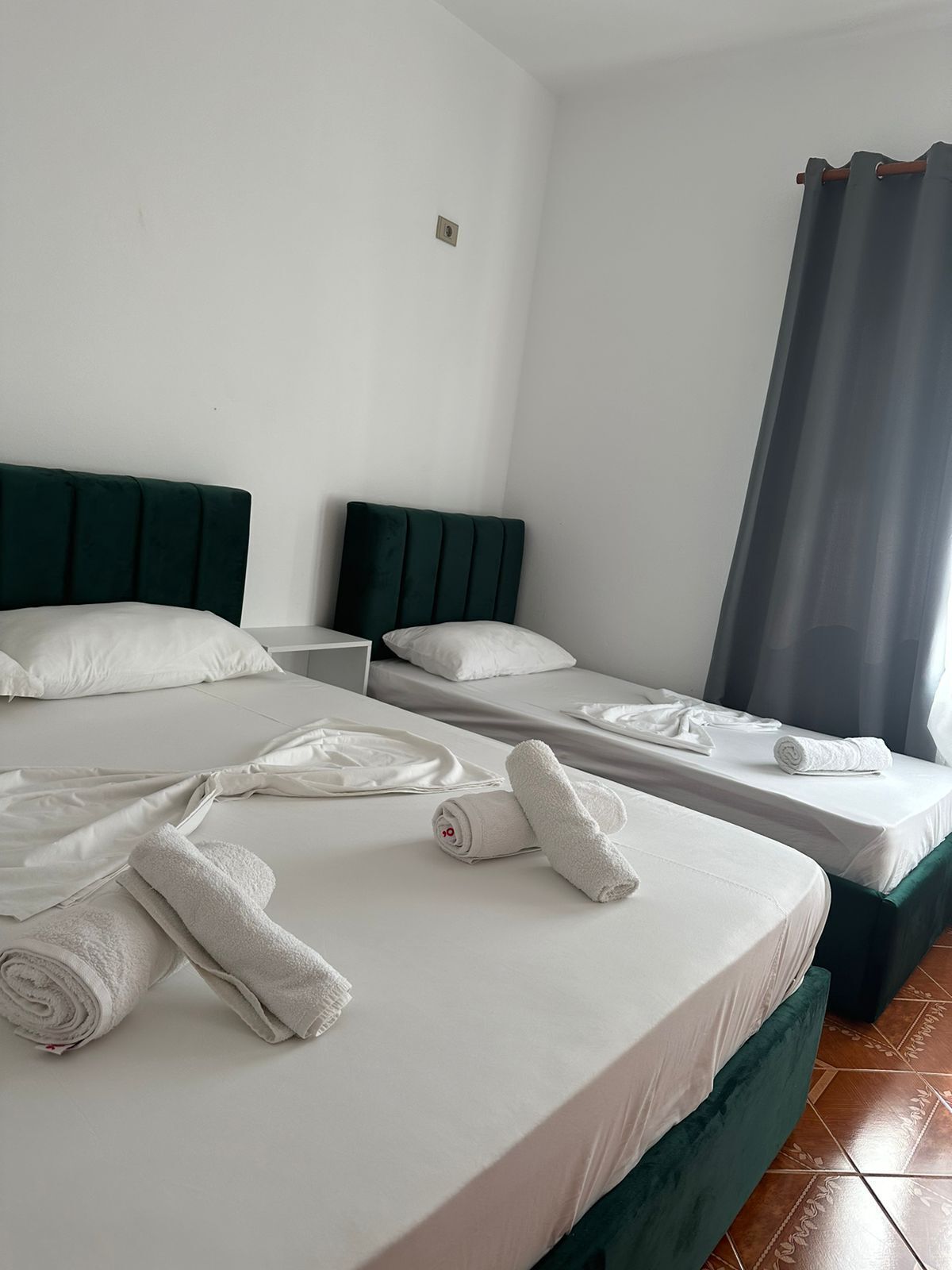 Habitación de hotel con dos camas, cada una con cabecera verde y ropa de cama blanca. Hay toallas bien dobladas sobre las camas.