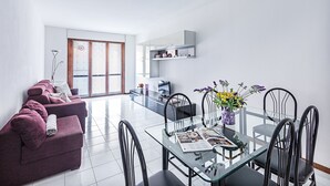 Ein modernes Wohnzimmer mit einem Glastisch, einem violetten Sofa und einem Fernseher im Hintergrund.