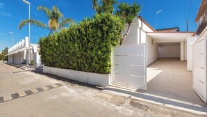 A residential street with a white gate, a paved driveway, and a row of white buildings with a covered parking area. - 3960 Villa Colle Azzurro by Barbarhouse (Porto Cesareo)