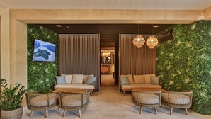 Un hall con zona de estar, sofás y sillones, un televisor montado en una pared verde y vistas al interior.