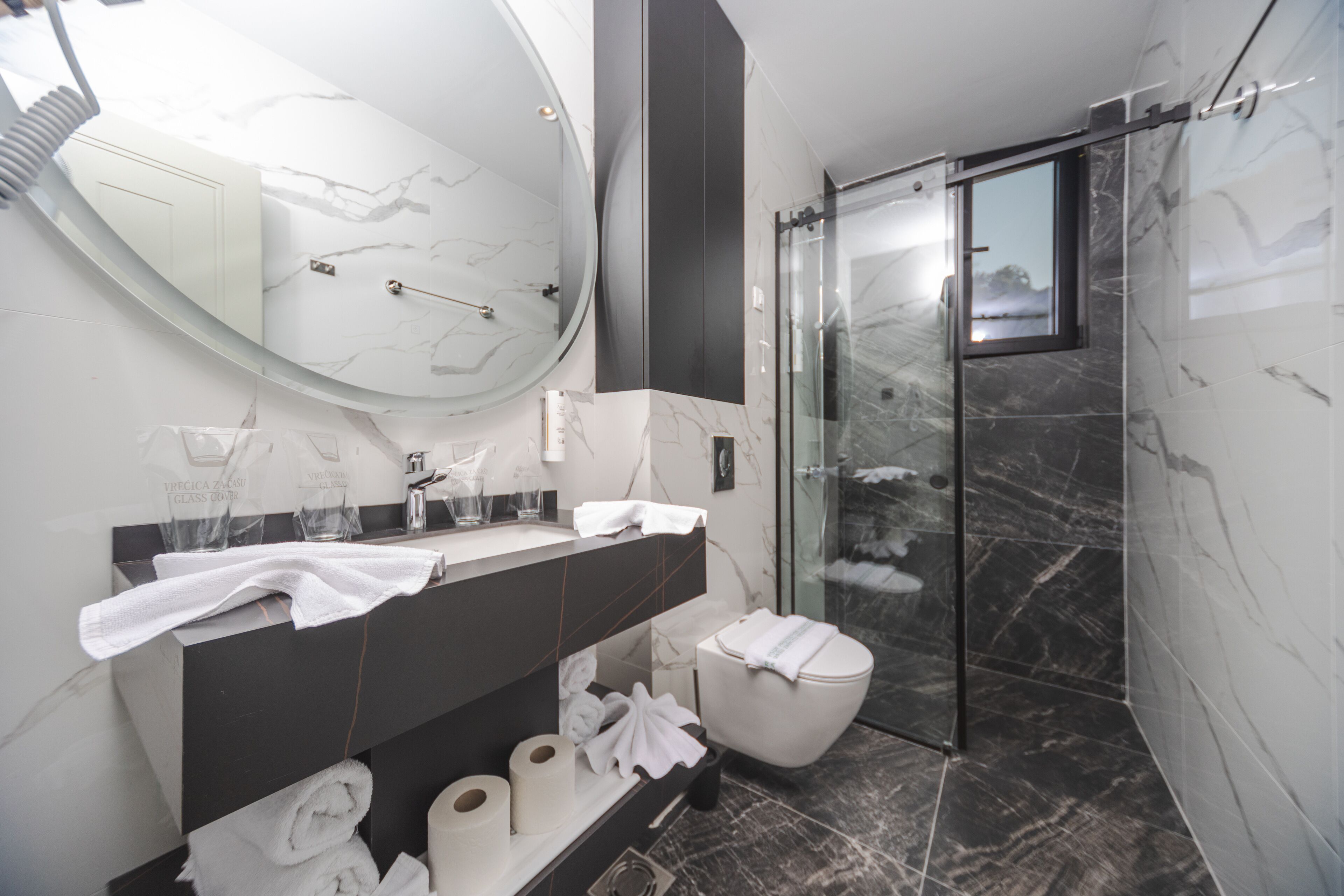 A modern bathroom with a marble vanity, a glass shower enclosure, and a toilet.