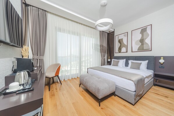 A modern hotel room with a large bed, a desk with a coffee maker, a chair, and artwork on the walls. - Hotel kingStone Budva (Przno)
