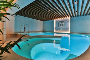 A modern indoor pool with clear blue water, a wooden ceiling, and a logo on the wall.