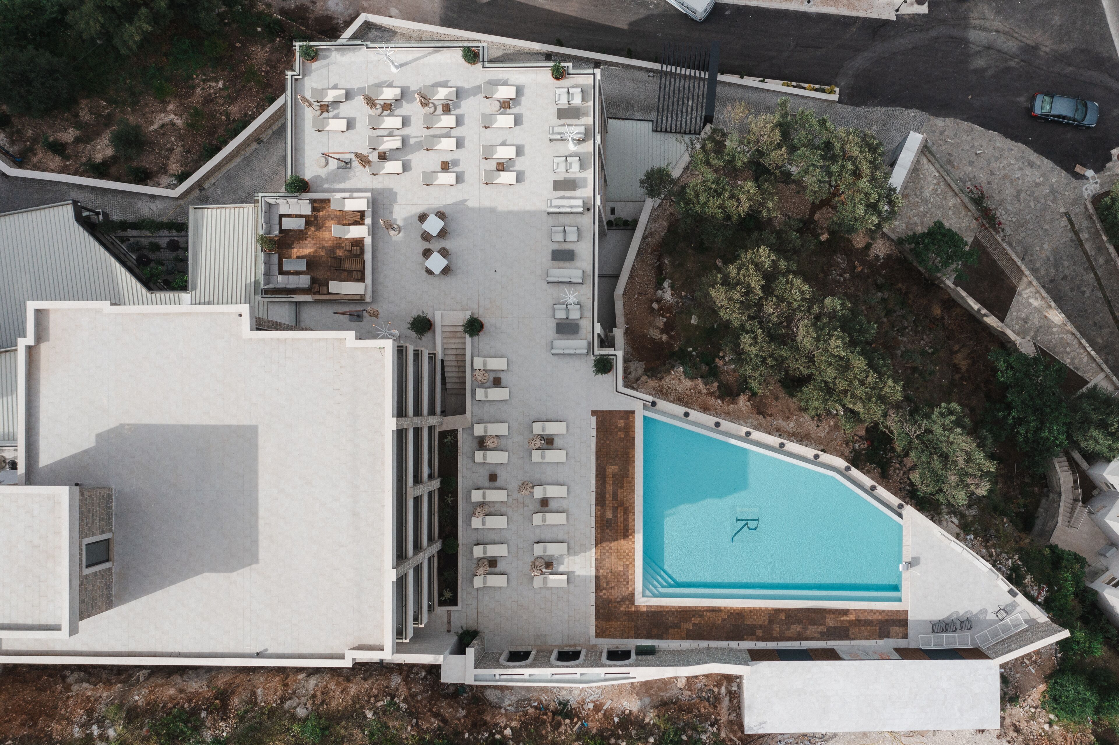 An aerial view of a hotel with a rooftop pool, outdoor seating area, and a landscaped garden.