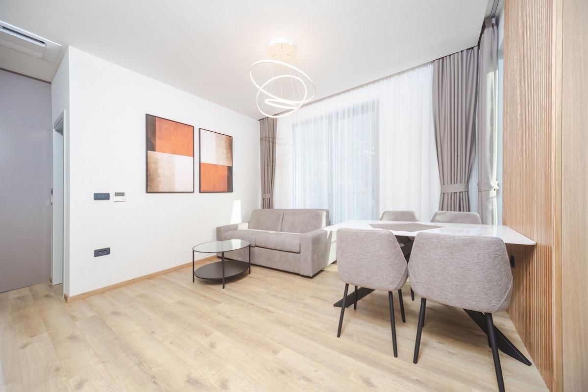 A modern living room with a sofa, a dining table with chairs, a round coffee table, and a contemporary light fixture.