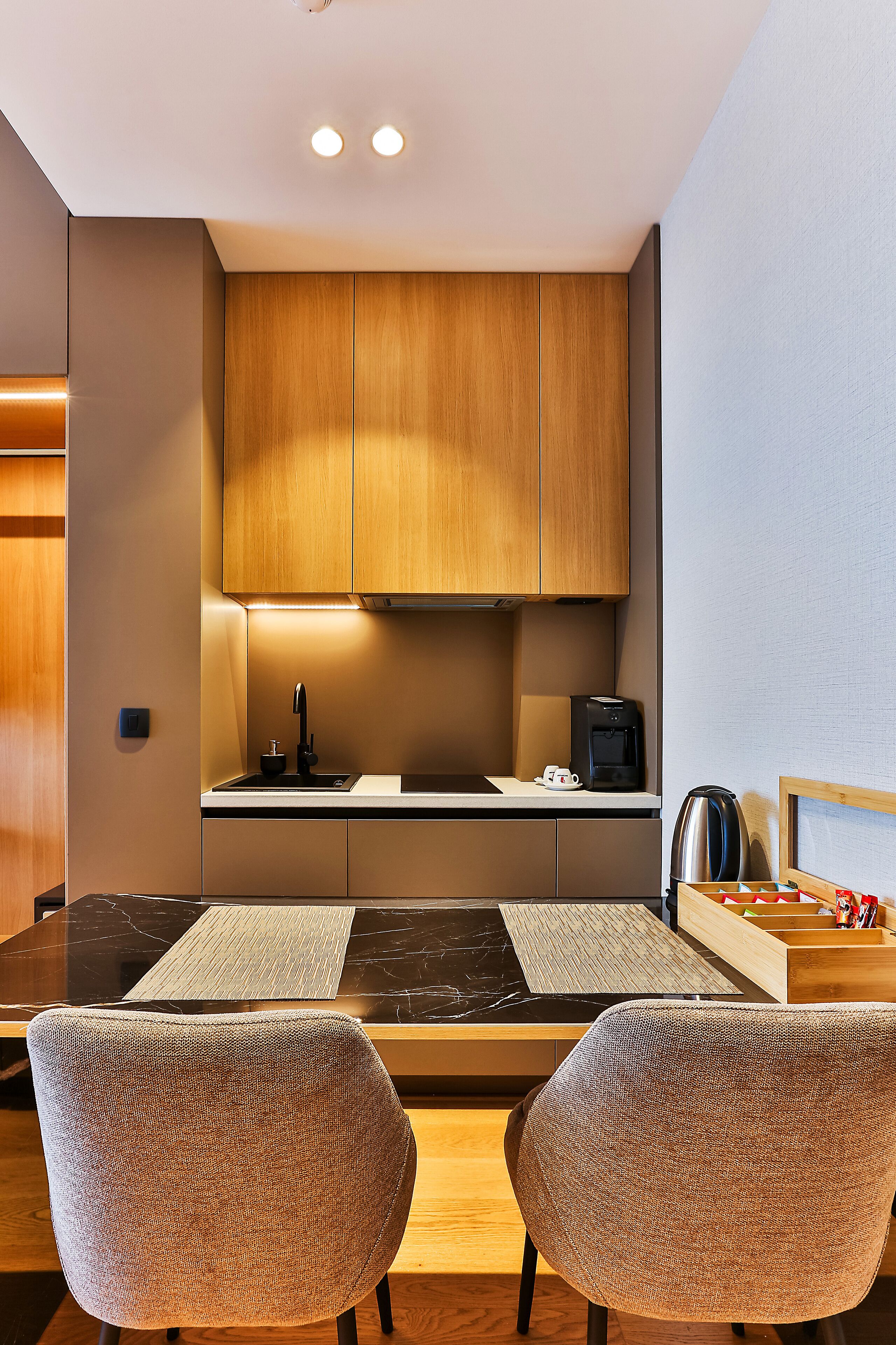 A modern kitchen with wooden cabinets, a black countertop, and two chairs.