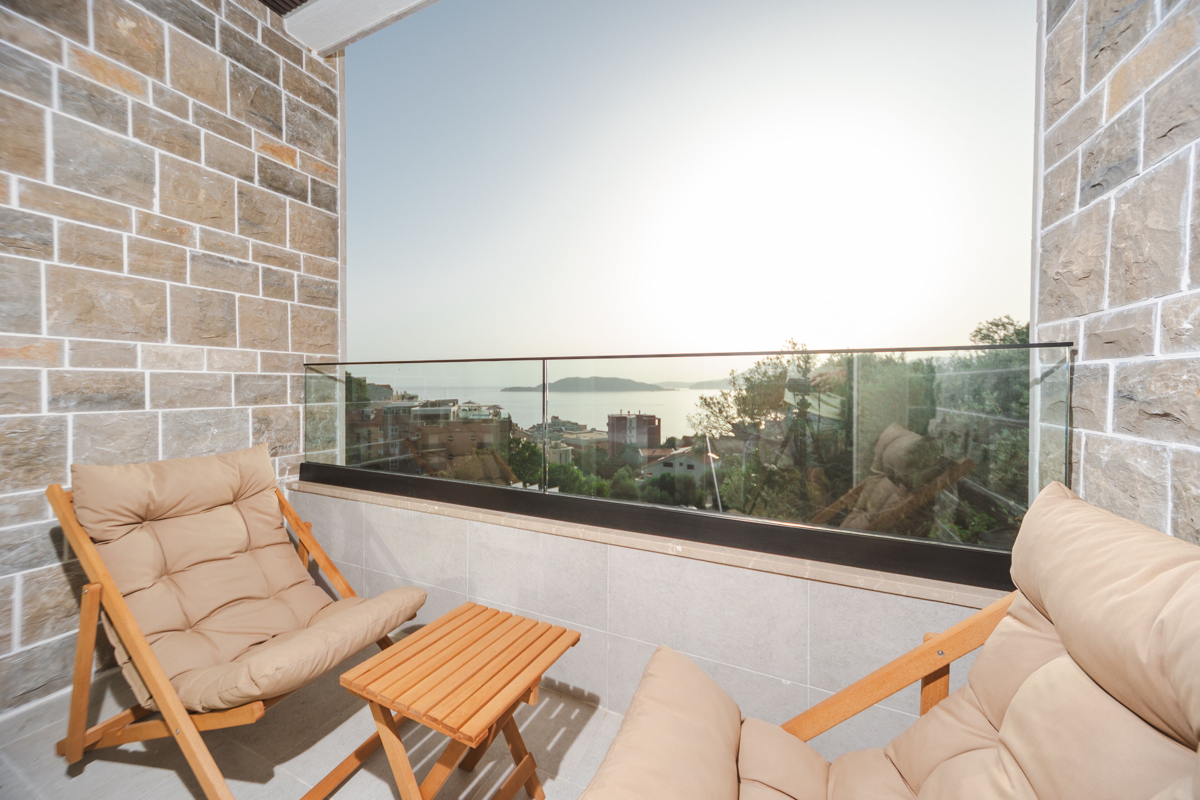 A balcony with a stone wall, two cushioned chairs, and a wooden table.
