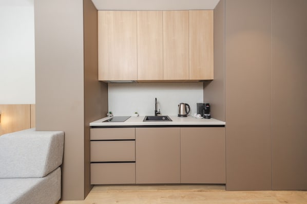 A compact kitchen with wooden cabinets, a sink, a kettle, and a small countertop. - Hotel kingStone Budva (Przno)