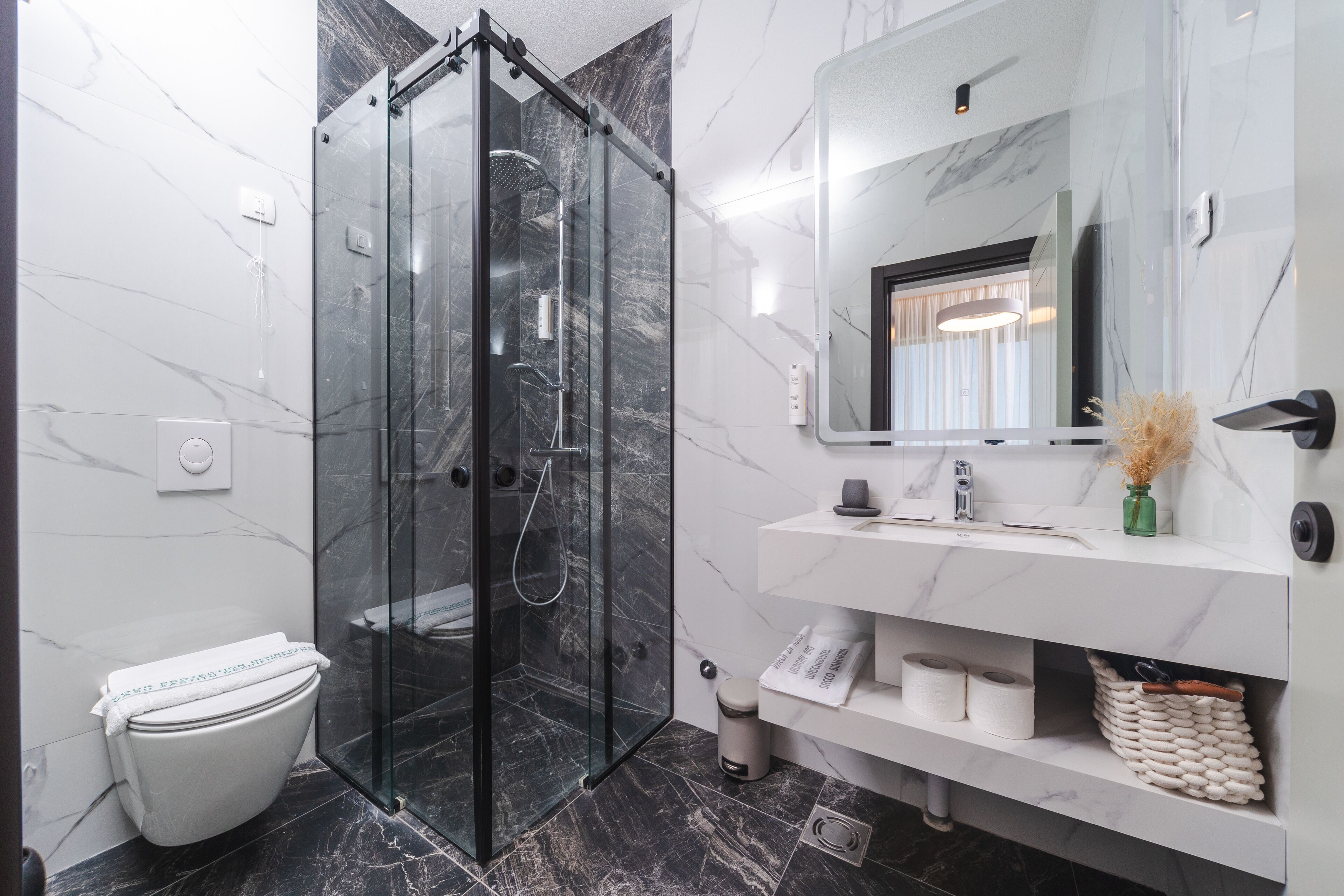 A modern bathroom with a glass-enclosed shower, a white toilet, and a marble-tiled floor.