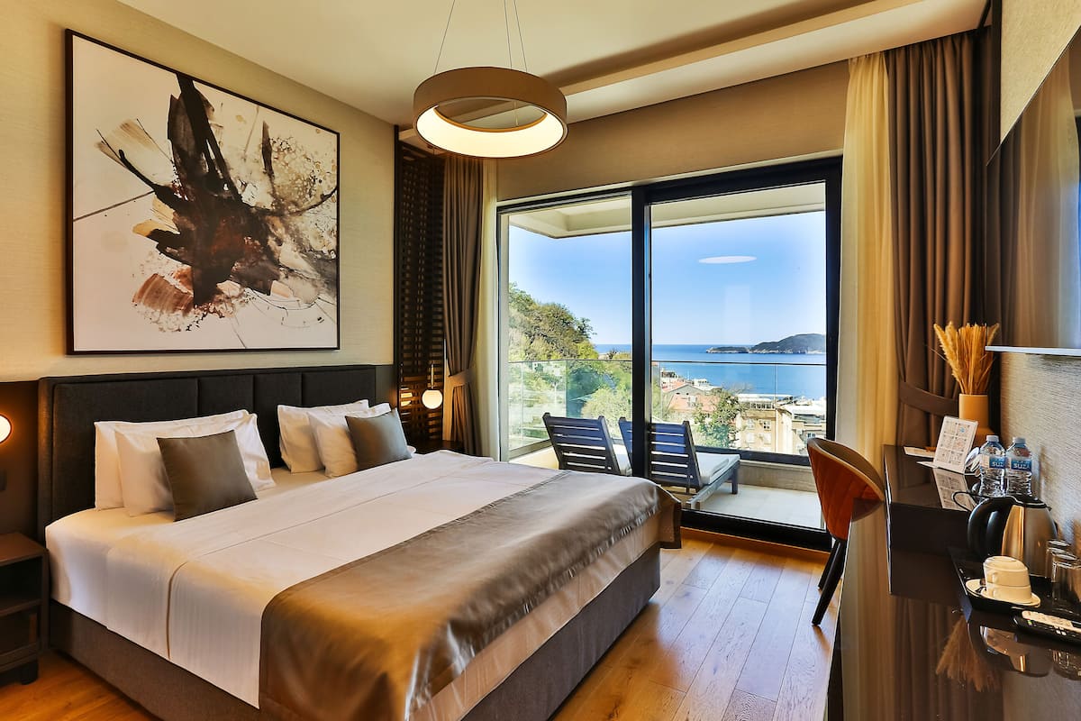 A modern hotel room with a large bed, a desk with a coffee maker, and a view of the sea.