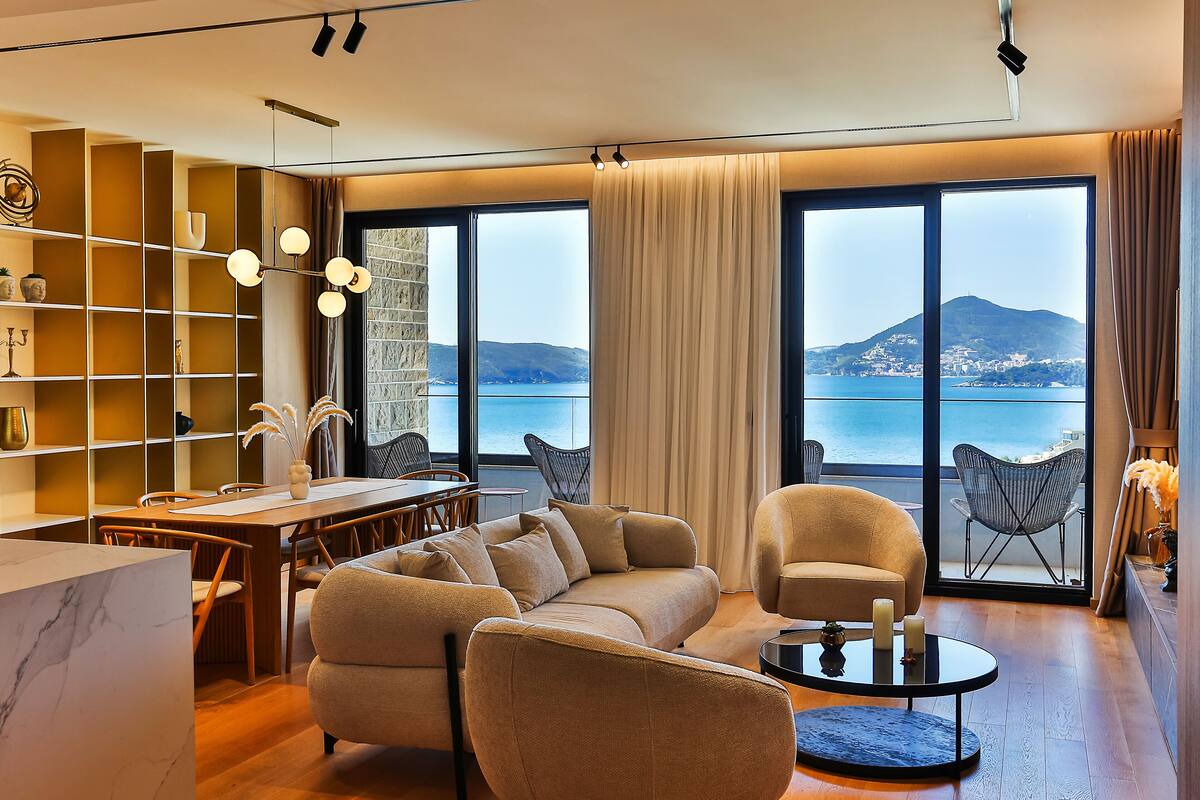 A modern living room with a sofa, armchairs, a dining table, and a view of the sea.