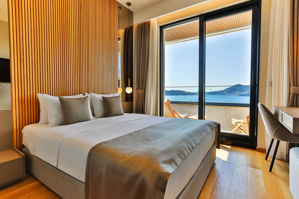 A modern hotel room with a large bed, a desk, and a view of the sea.