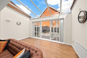 Relax in a spacious living area with a high ceiling and skylight, featuring a comfortable sofa and sliding glass doors to an outdoor patio.