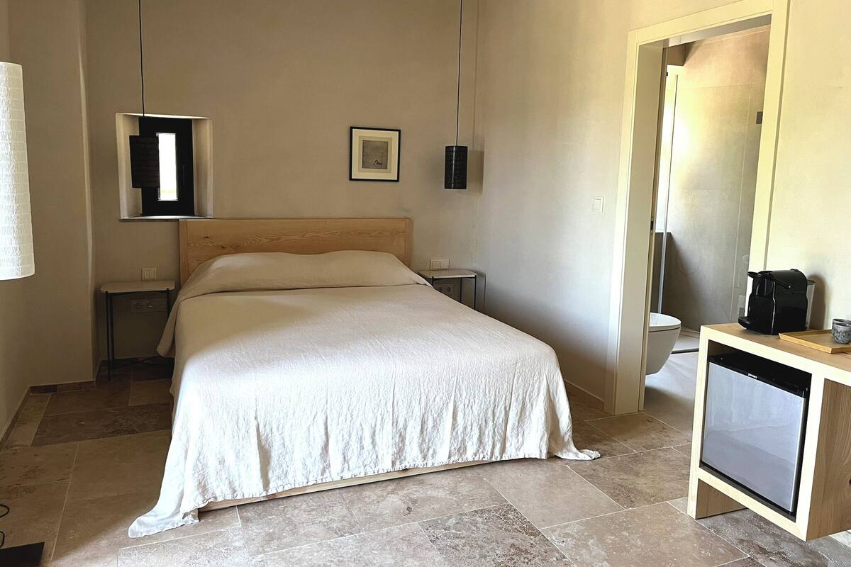 Ein Hotelzimmer mit einem Bett, Nachttischen, einem kleinen Nachtschränkchen, einem Spiegel und einer Kaffeemaschine.