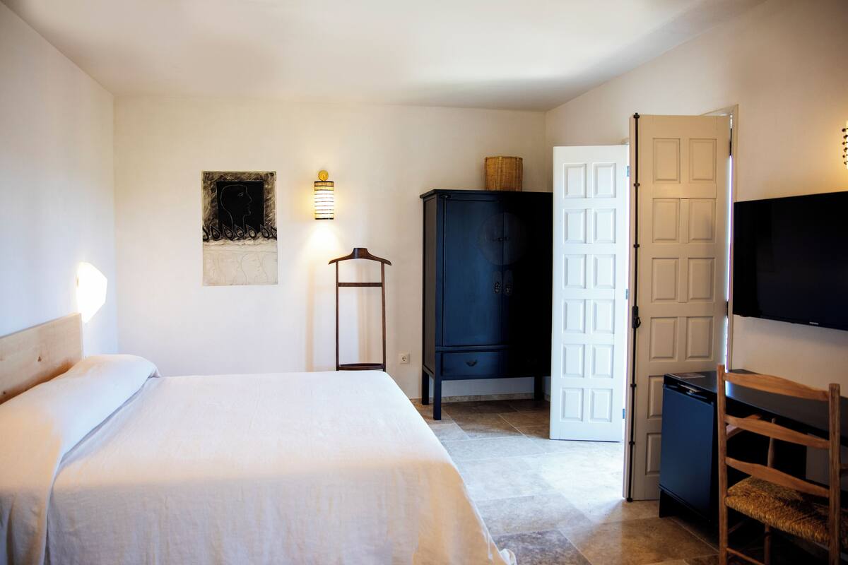 Ein Schlafzimmer mit Bett, Kleiderschrank, Schreibtisch mit Stuhl, Fernseher und einer Tür.