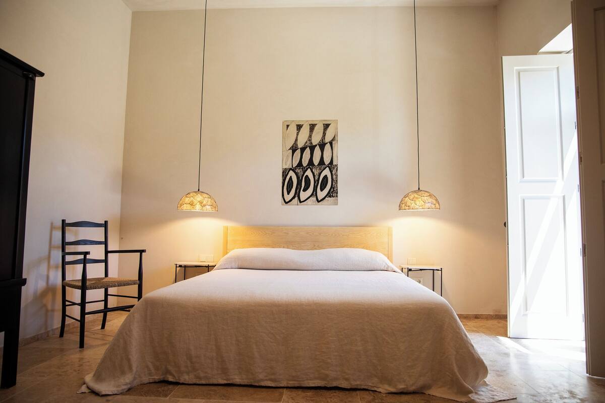 Ein Schlafzimmer mit einem großen Bett, einem Sessel, einem Wandbild und zwei Wandlampen.