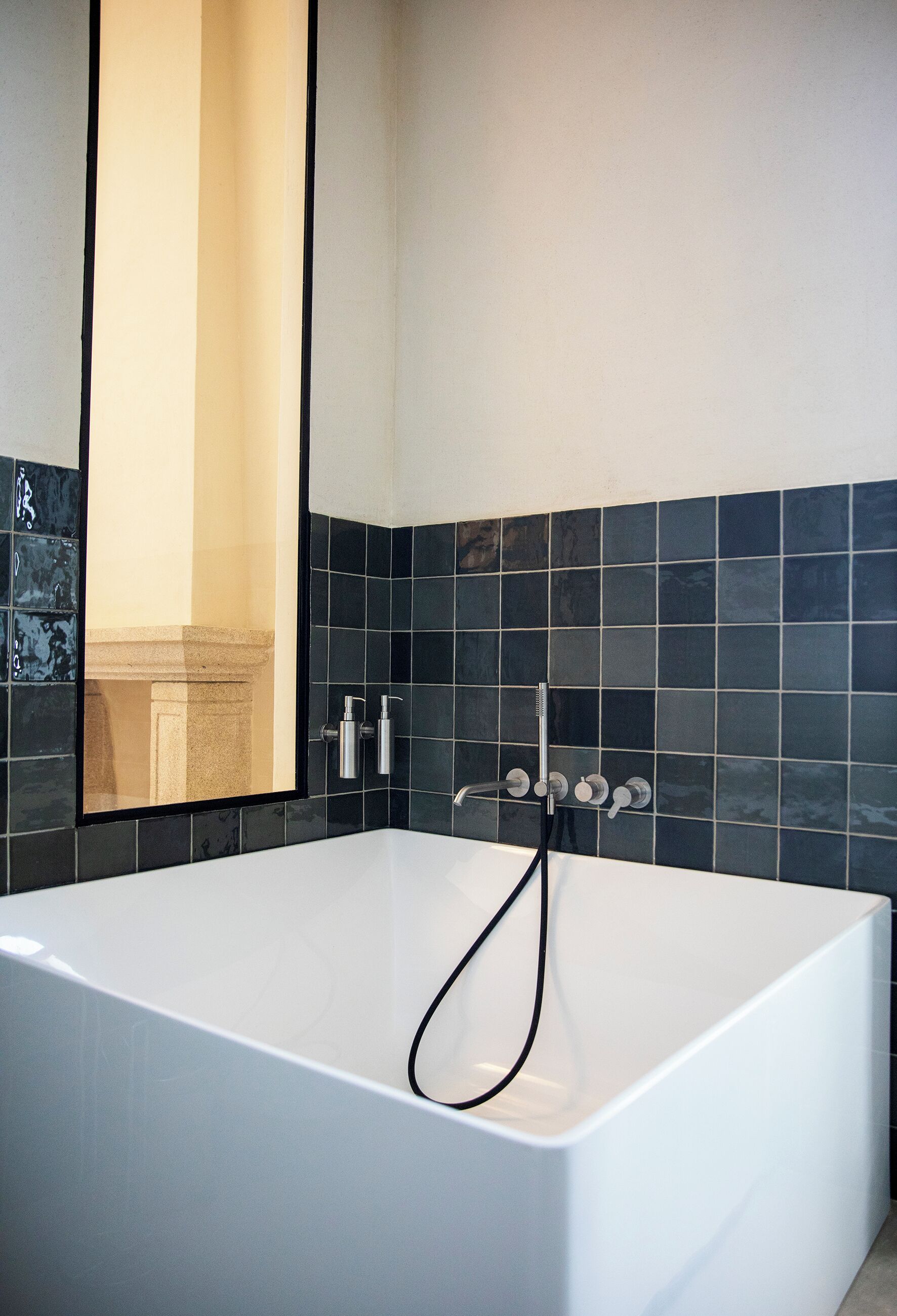 Un baño moderno con una bañera grande, un espejo y paredes con azulejos negros.