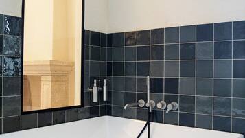 Un baño moderno con una bañera grande, un espejo y paredes con azulejos negros.