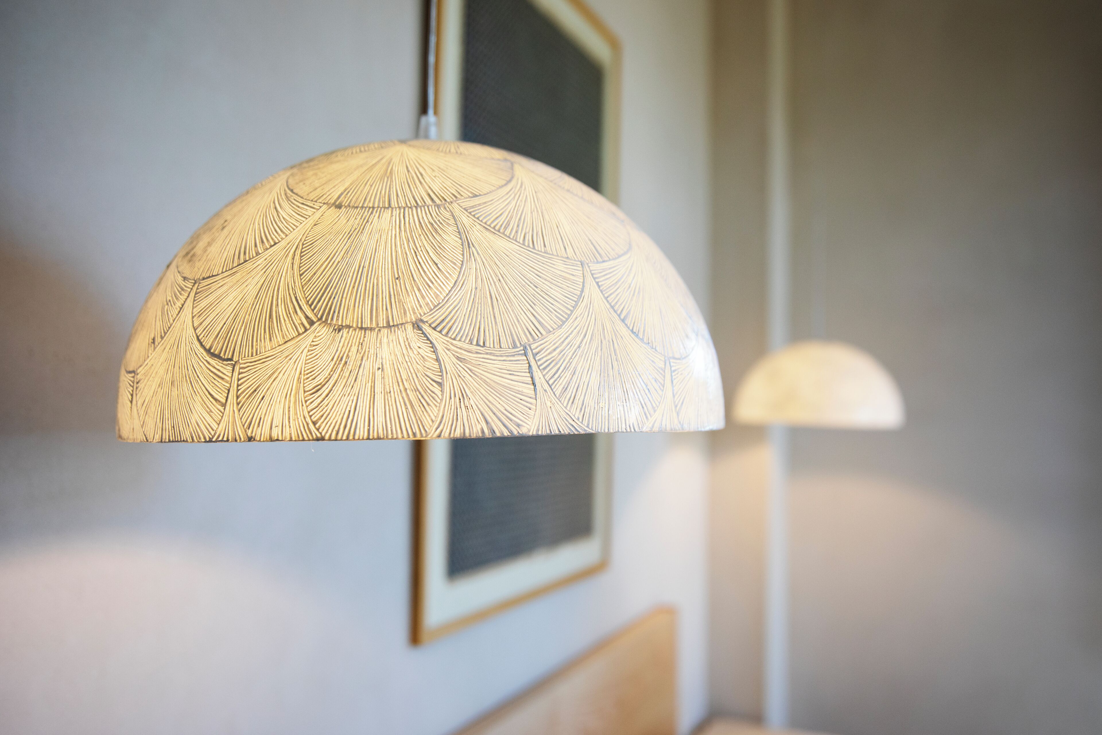 Une pièce avec un lampadaire au plafond orné d’un motif de feuilles, un tableau encadré accroché au mur et un lit doté d’une tête de lit en bois.