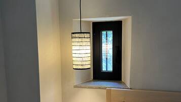 Un dormitorio con una pequeña ventana, una mesita de noche y una lámpara colgante.
