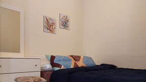 Un dormitorio con cama, mesita de noche, silla, cómoda y dos cuadros en la pared.