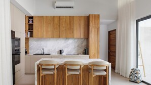 Una cocina moderna con armarios de madera, salpicadero de mármol, horno empotrado y una zona de comedor con tres sillas.