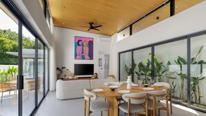 Un comedor moderno con una mesa y sillas de madera, un televisor de pantalla plana al fondo y ventanas amplias que ofrecen vistas al verdor.