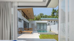 Habitación de hotel moderna con un gran ventanal que da a un balcón, una piscina y vistas del entorno.