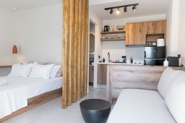 Ett modernt hotellrum med en väggpanel i trä, ett litet kök, en säng och en sittgrupp.