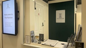 A reception desk at The Norton Seaton Carew hotel with a digital welcome screen, reception area, and informational sign. - The Norton (Hartlepool)