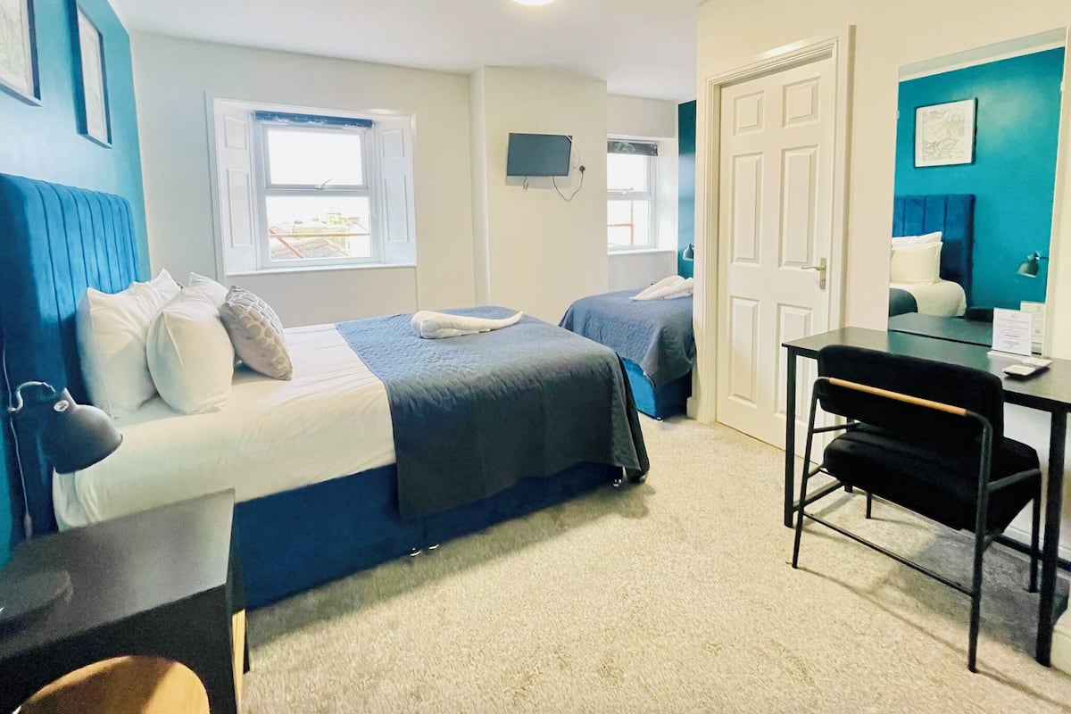 A bedroom with two beds, a desk, a chair, a TV, and a door.