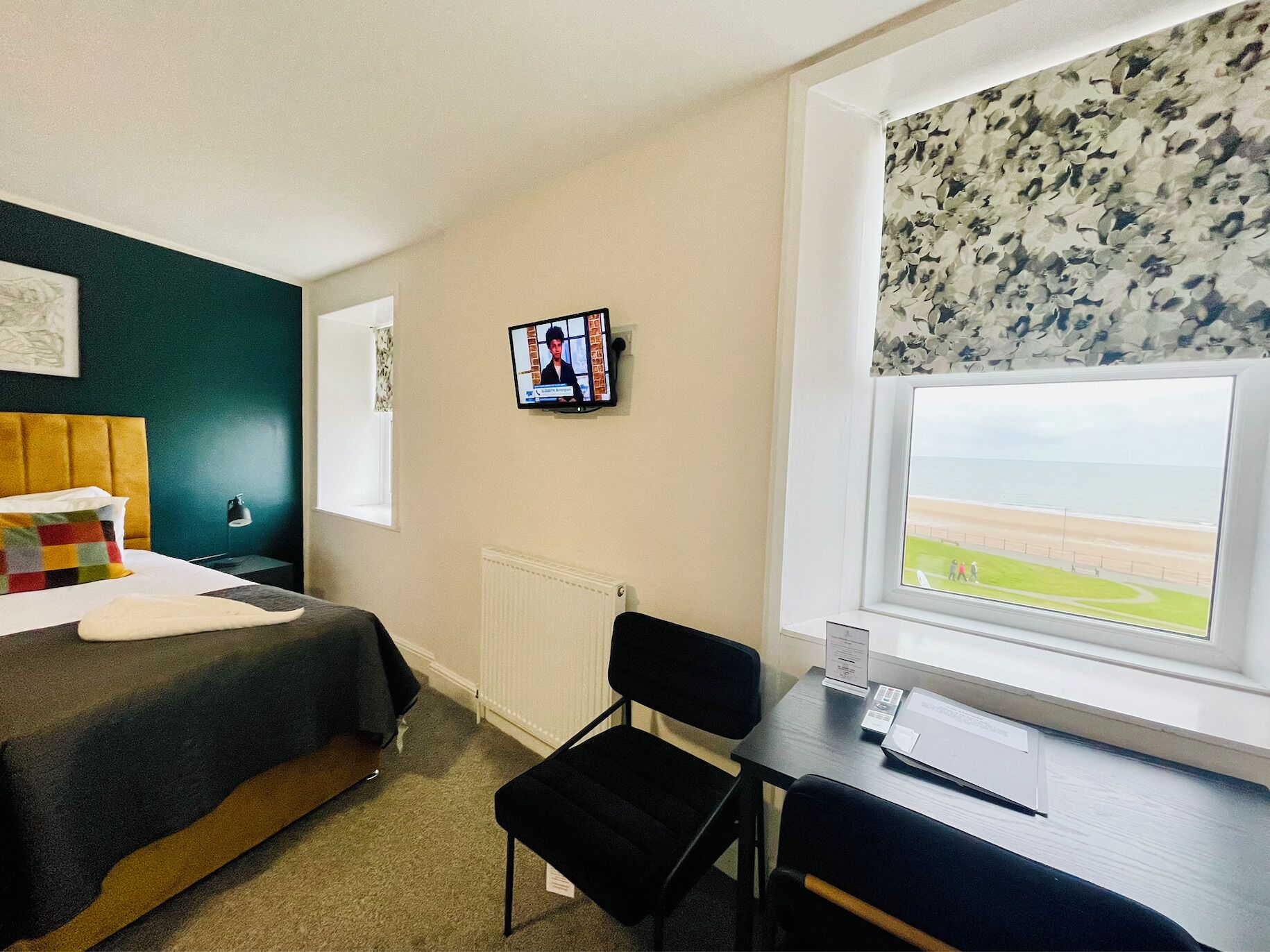 Une chambre d’hôtel comprenant un lit, un bureau, une chaise, une télévision, une fenêtre donnant sur la plage et un radiateur.