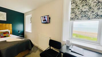 Une chambre d’hôtel comprenant un lit, un bureau, une chaise, une télévision, une fenêtre donnant sur la plage et un radiateur.