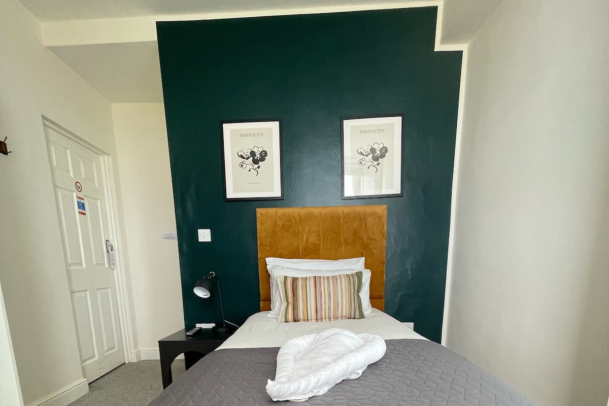 A neatly made bed with a grey quilt, a wooden headboard, and two framed pictures on the wall.