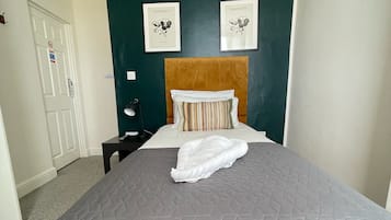 A neatly made bed with a grey quilt, a wooden headboard, and two framed pictures on the wall.