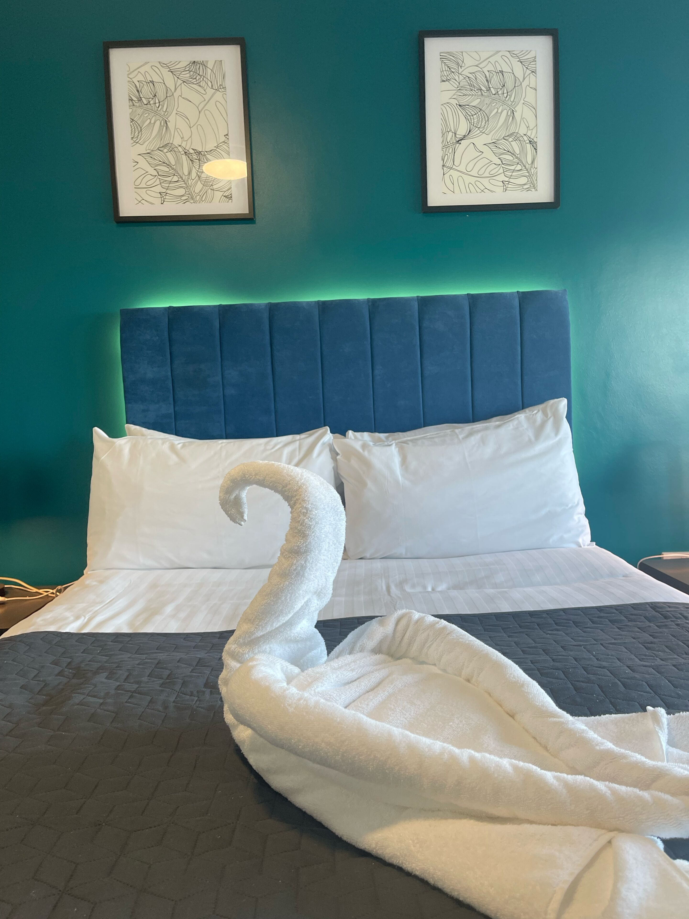 A bed with white pillows and a swan-shaped towel, teal walls, and framed artwork.