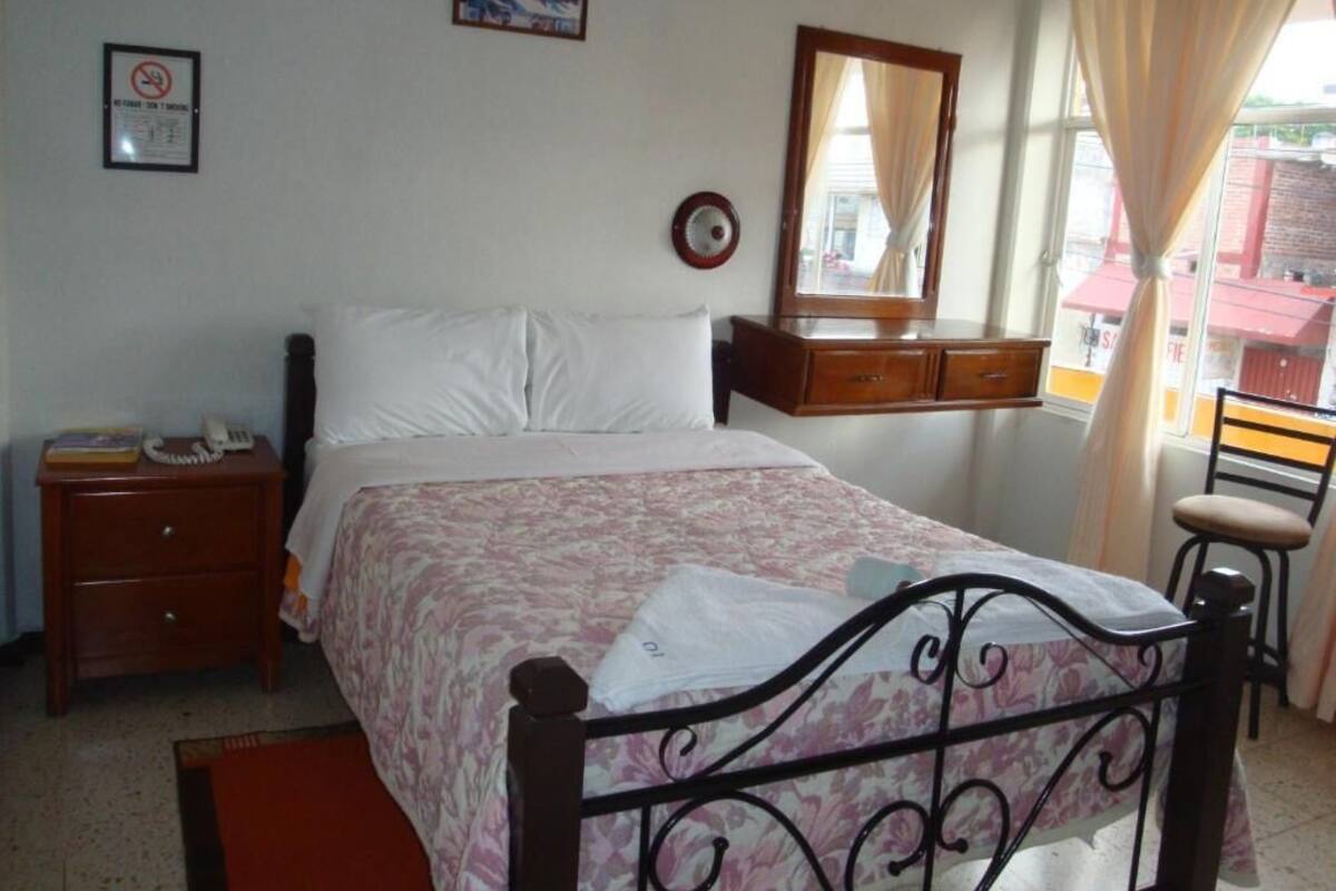 A bedroom with a bed, a nightstand, a dresser, a mirror, and a window with curtains.