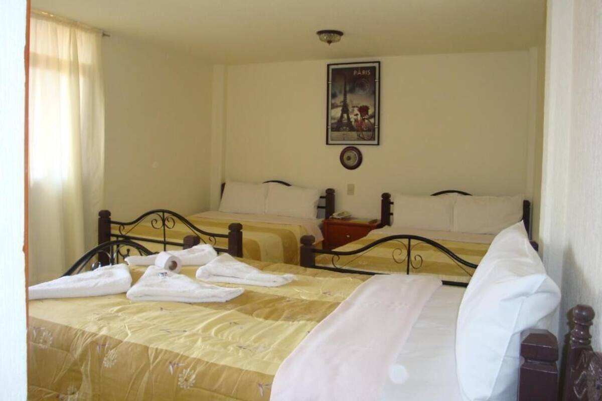 A hotel room with two beds, a poster of the Eiffel Tower, and a bedside table with a lamp.