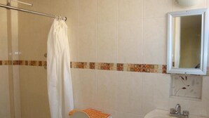 A bathroom with a shower, toilet, sink, and a mirror. - Hotel Los Angeles  (Tulancingo)