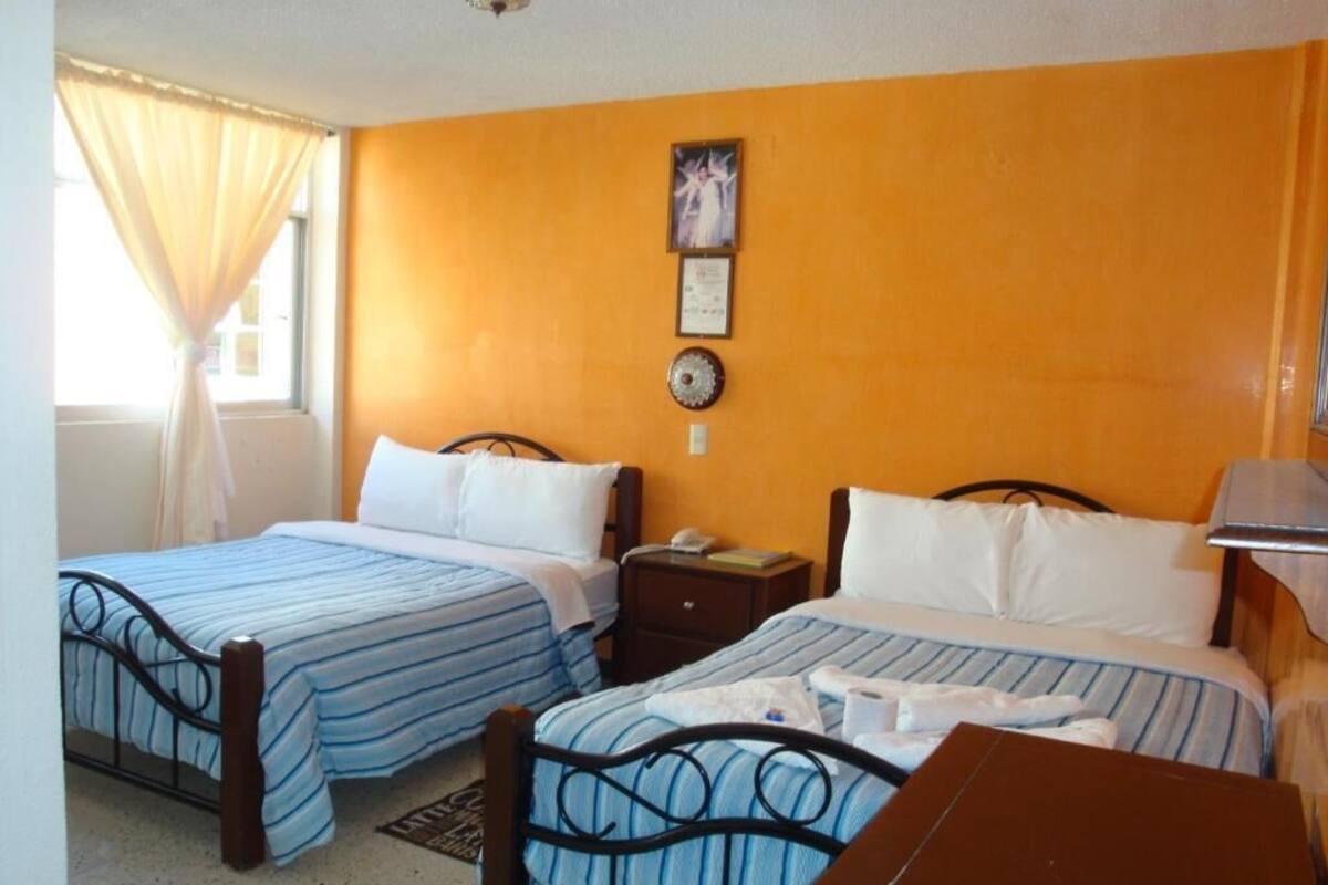 A room with two beds, a wooden table, a nightstand, and a window with curtains.