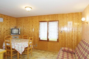 Una habitación con paredes de paneles de madera, una mesa de comedor con sillas, un televisor y un sofá.