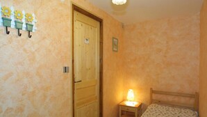 A small bedroom with a wooden door, a bedside table with a lamp, and a bed with a patterned bedspread. - Wifi, Ground floor, tv, 25m², Les Gets (Les Gets)