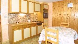 A compact kitchen with wooden cabinets, a tiled backsplash, a microwave, and a dining table with chairs. - Wifi, Ground floor, tv, 25m², Les Gets (Les Gets)