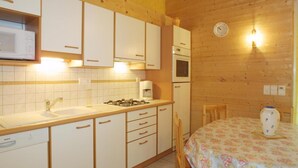 A compact kitchen with white cabinets, a Bosch dishwasher, a gas stove, and a microwave. There's a wooden dining table with a floral tablecloth and a vase on it. - Wifi, Ground floor, terrace, tv, 58m², Les Gets (Les Gets)