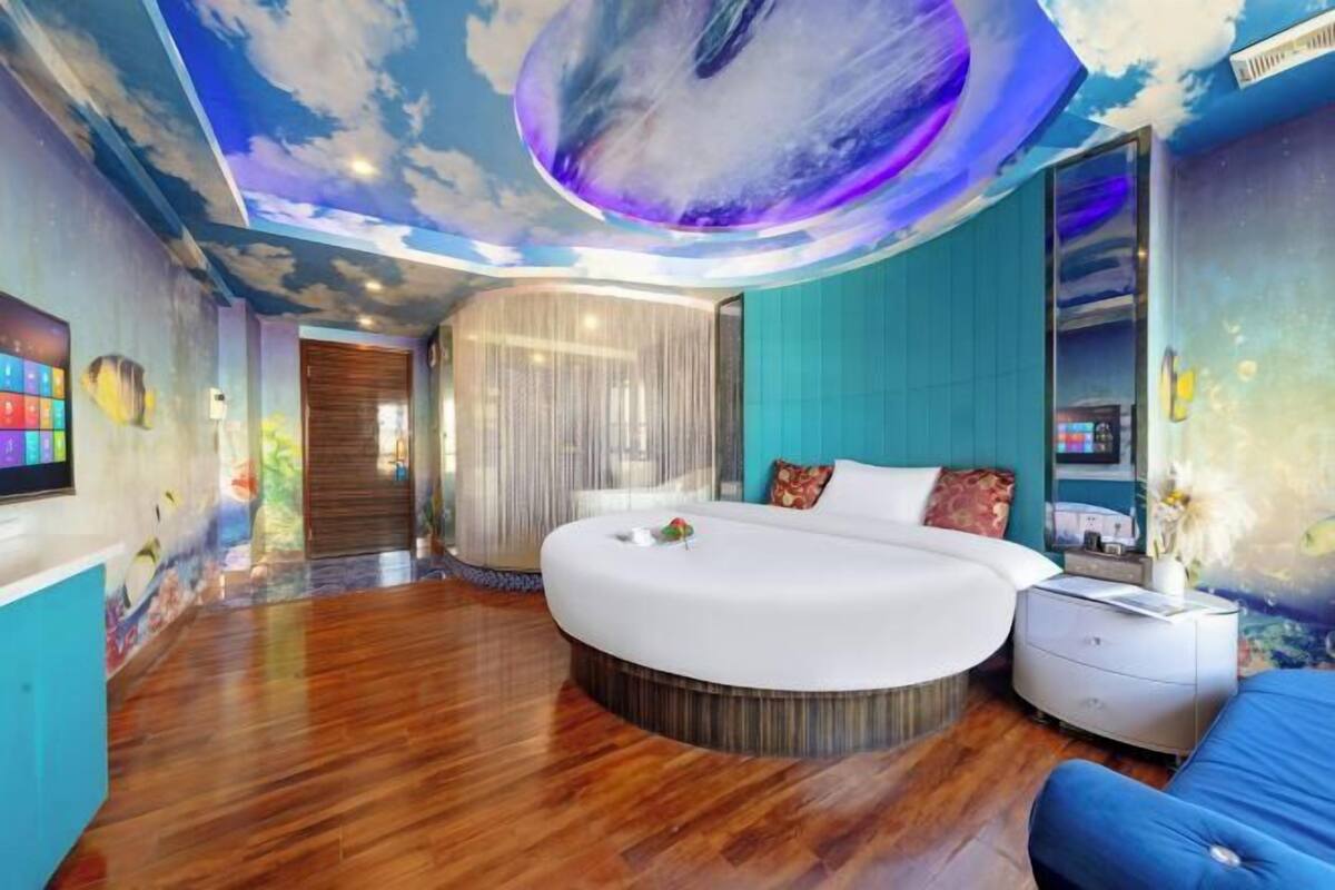 A modern bedroom with a round bed, a nightstand, a blue sofa, and a mural on the ceiling.