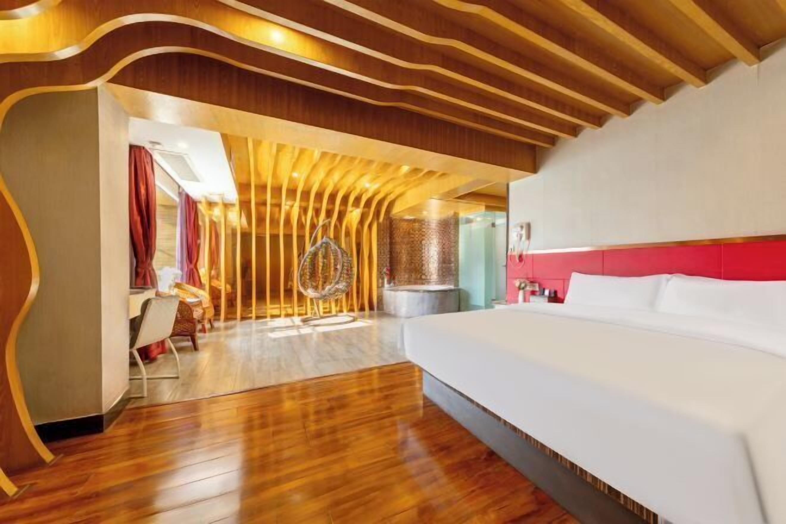 A modern hotel room with a wooden ceiling, a large bed, and a dining area with a chair and table.